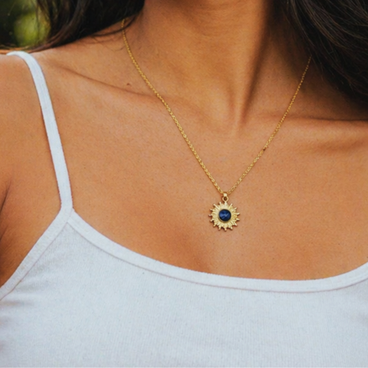 Woman wearing a gold sun necklace with a blue lapis lazuli pendant