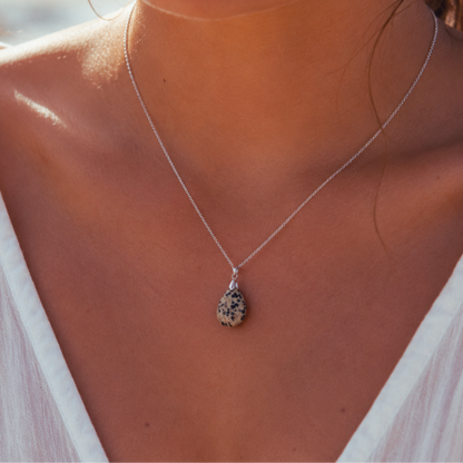 A close-up lifestyle shot of a woman wearing a delicate silver chain necklace with a teardrop-shaped natural Dalmatian Jasper Lifestyle pendant featuring black and white marbled patterns.