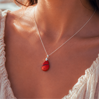 A close-up lifestyle shot of a woman wearing a silver chain necklace with a teardrop-shaped red jasper pendant featuring black marbled lines.