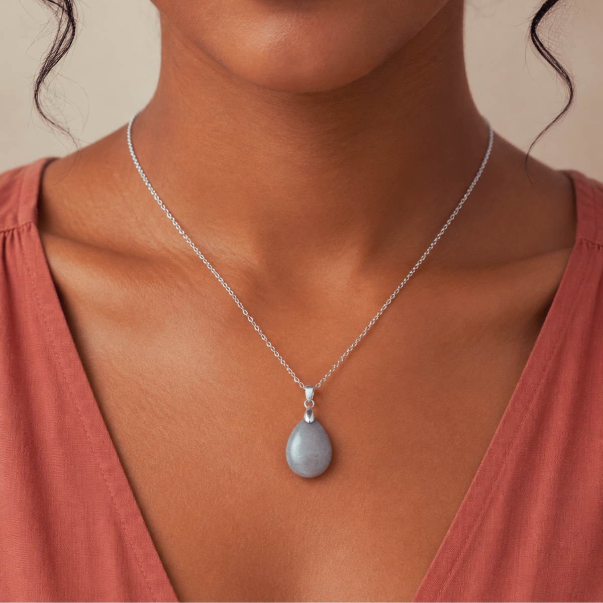 A close-up of a woman wearing a delicate silver chain necklace with a teardrop-shaped gray spectrloite stone pendant.