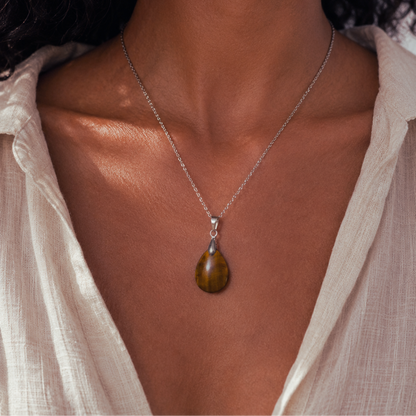 A close-up of a model wearing a silver chain necklace with a teardrop-shaped brown tiger's eye pendant, styled with a light beige linen top.